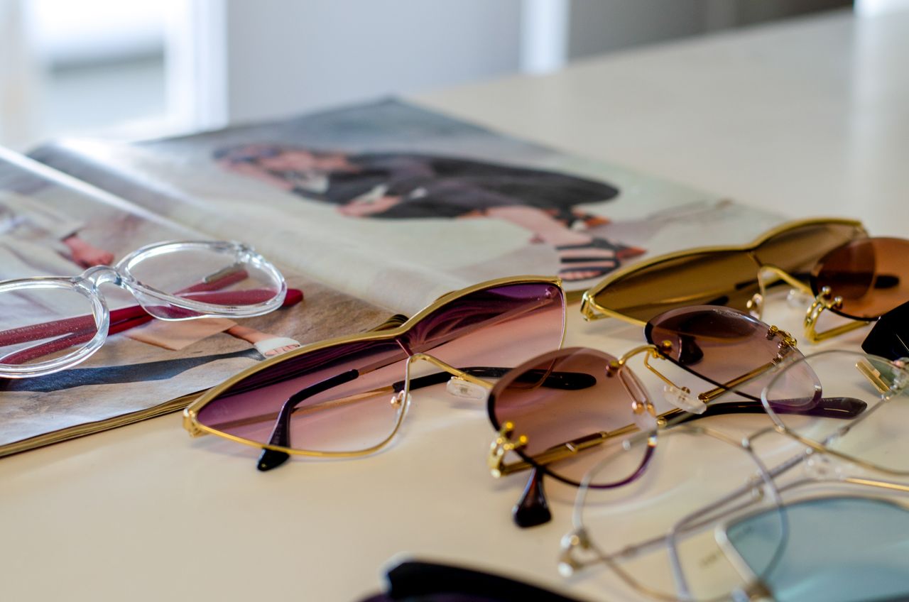 A variety of stylish sunglasses and reading glasses elegantly displayed on a table next to a fashion magazine.